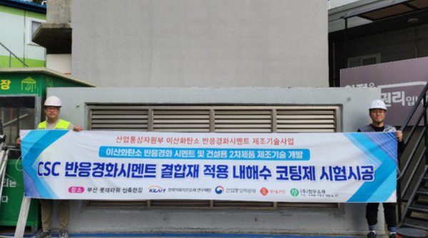 롯데건설 직원들이 부산 롯데타워 현장에서 ‘이산화탄소 반응경화 시멘트’를 활용한 코팅제를 시공하고 기념촬영을 했다. 사진=롯데건설